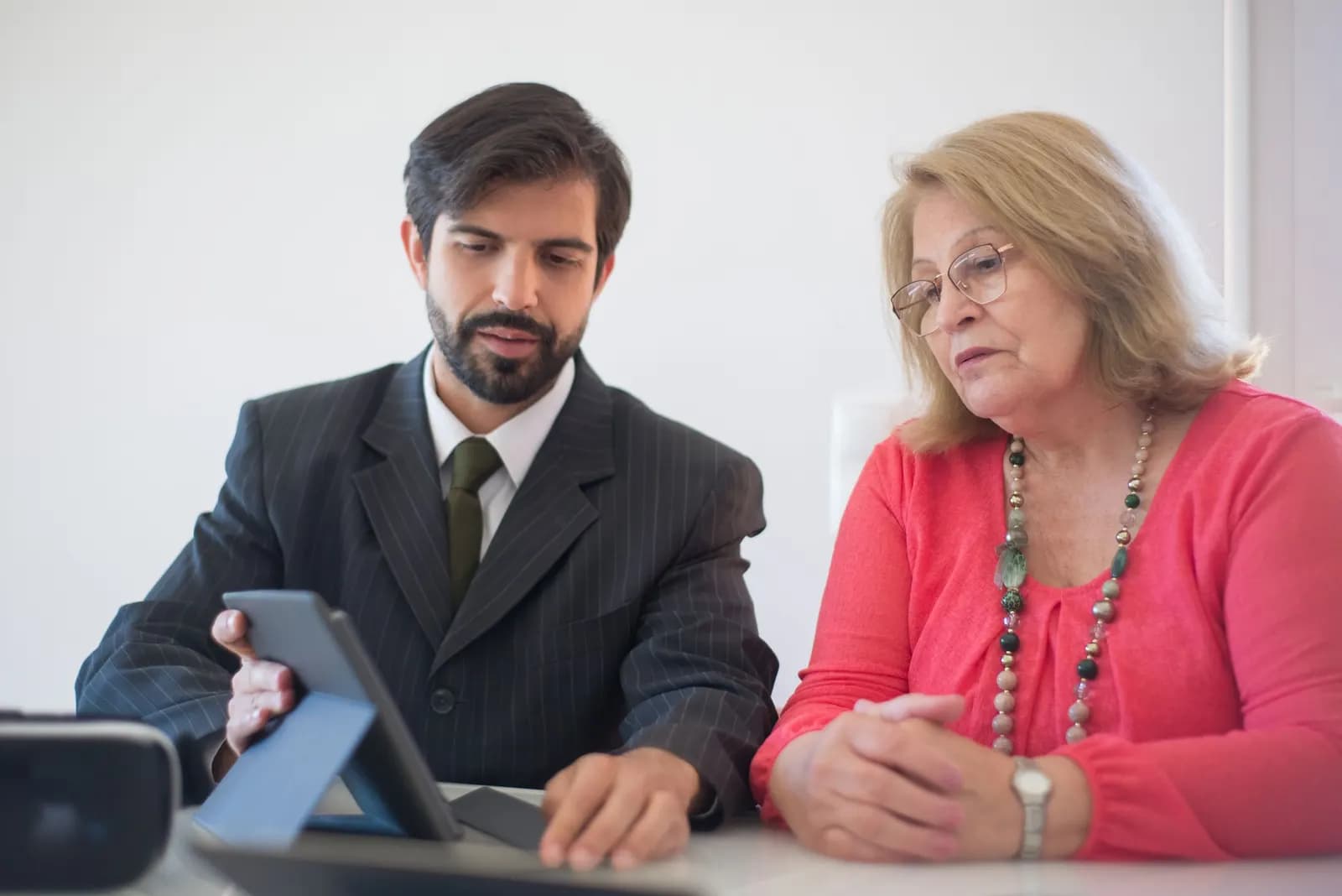 Adviser in a suit showing an older woman information on a tablet at a desk